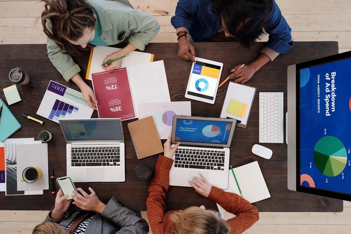 Free A diverse team collaborating on digital marketing strategies at a desk, using laptops and tablets. Stock Photo