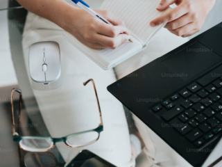 Person working remotely on a laptop at a desk with mouse and notebook.